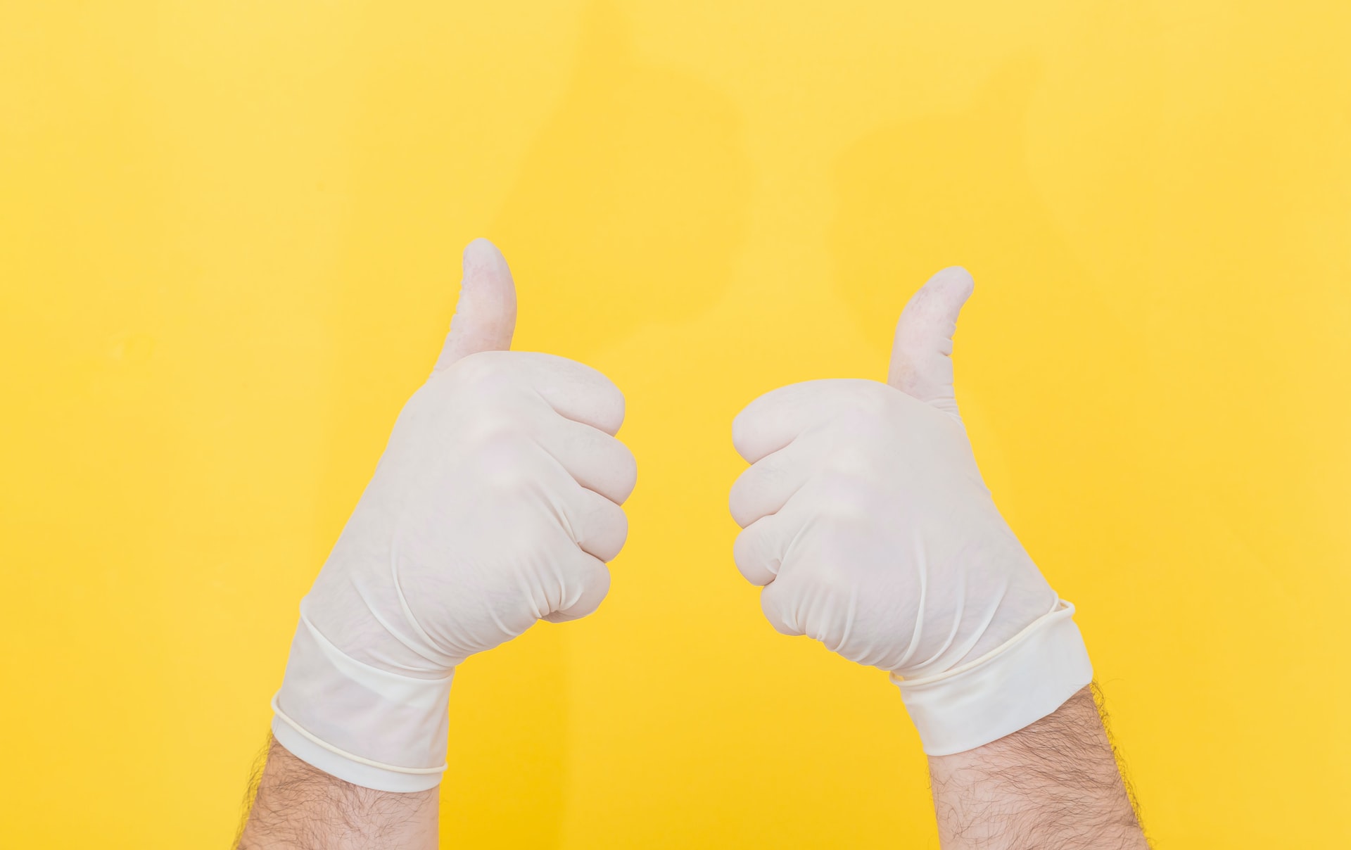 Two hands covered in latex gloves on a yellow background