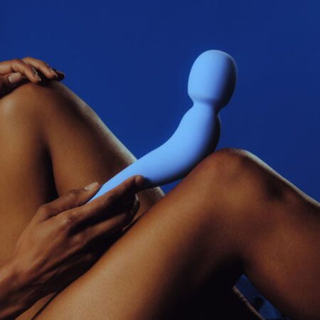 Dame Com Wand Vibrator in Periwinkle resting on a knee
