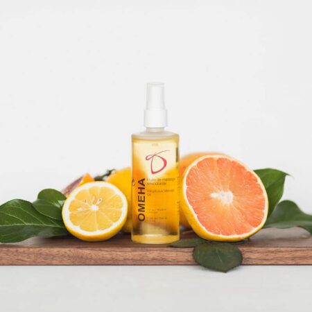 A clear container of Desirables Omeha Massage next to a cut orange and lemon on a table