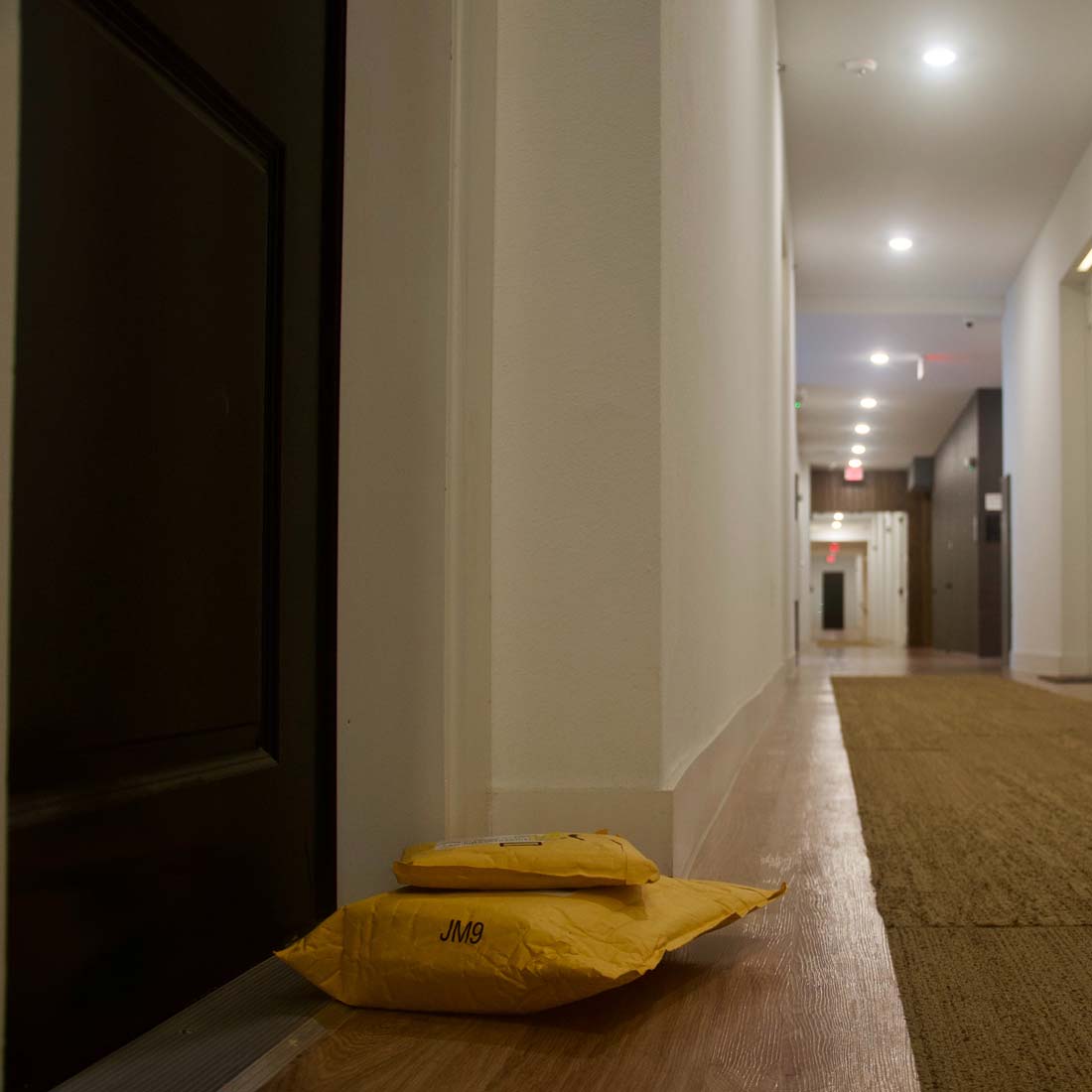 Two unlabeled envelope packages stacked on top of each other left outside a closed door in an apartment complex