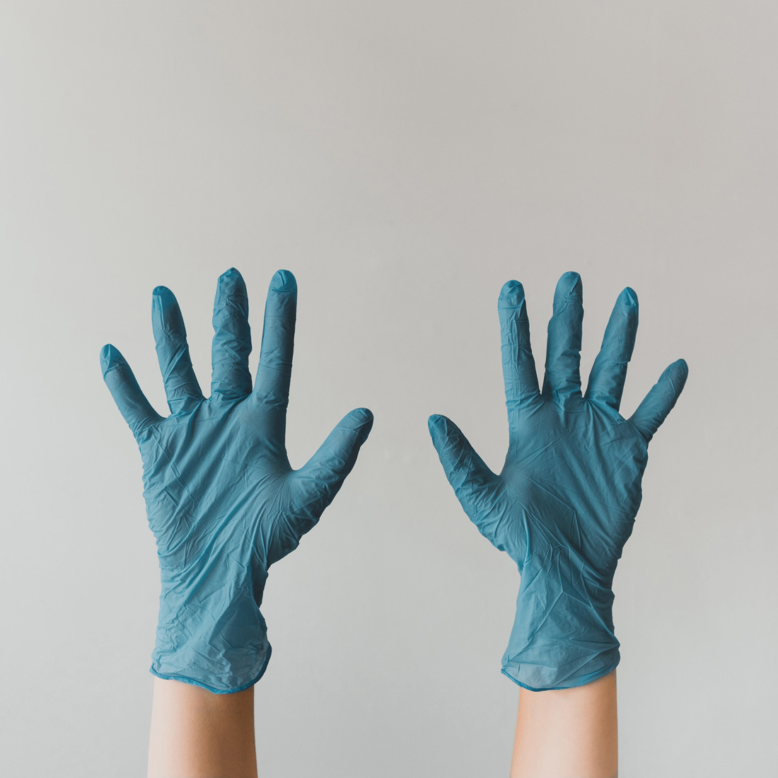 Two hands held in the air with aqua blue colored latex gloves