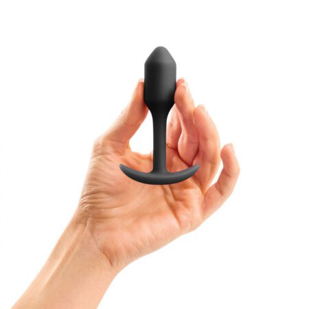 Hand holding a small sized, black Snug Plug butt plug covered withÂ  silicone on a white background