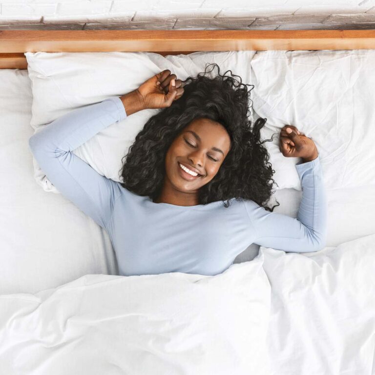 Woman lying in bed smiling with her hands near her head