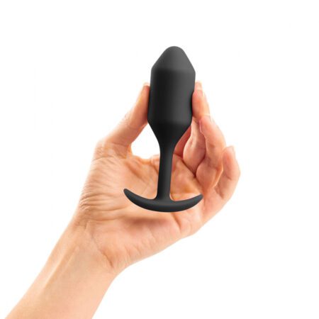 Hand holding a medium sized, black Snug Plug butt plug covered with  silicone on a white background
