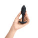 Hand holding a medium sized, vibrating, black Snug Plug butt plug covered with  silicone on a white background