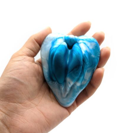 Hand holding the blue green labia shaped silicone grinder from Uberrime on a white background